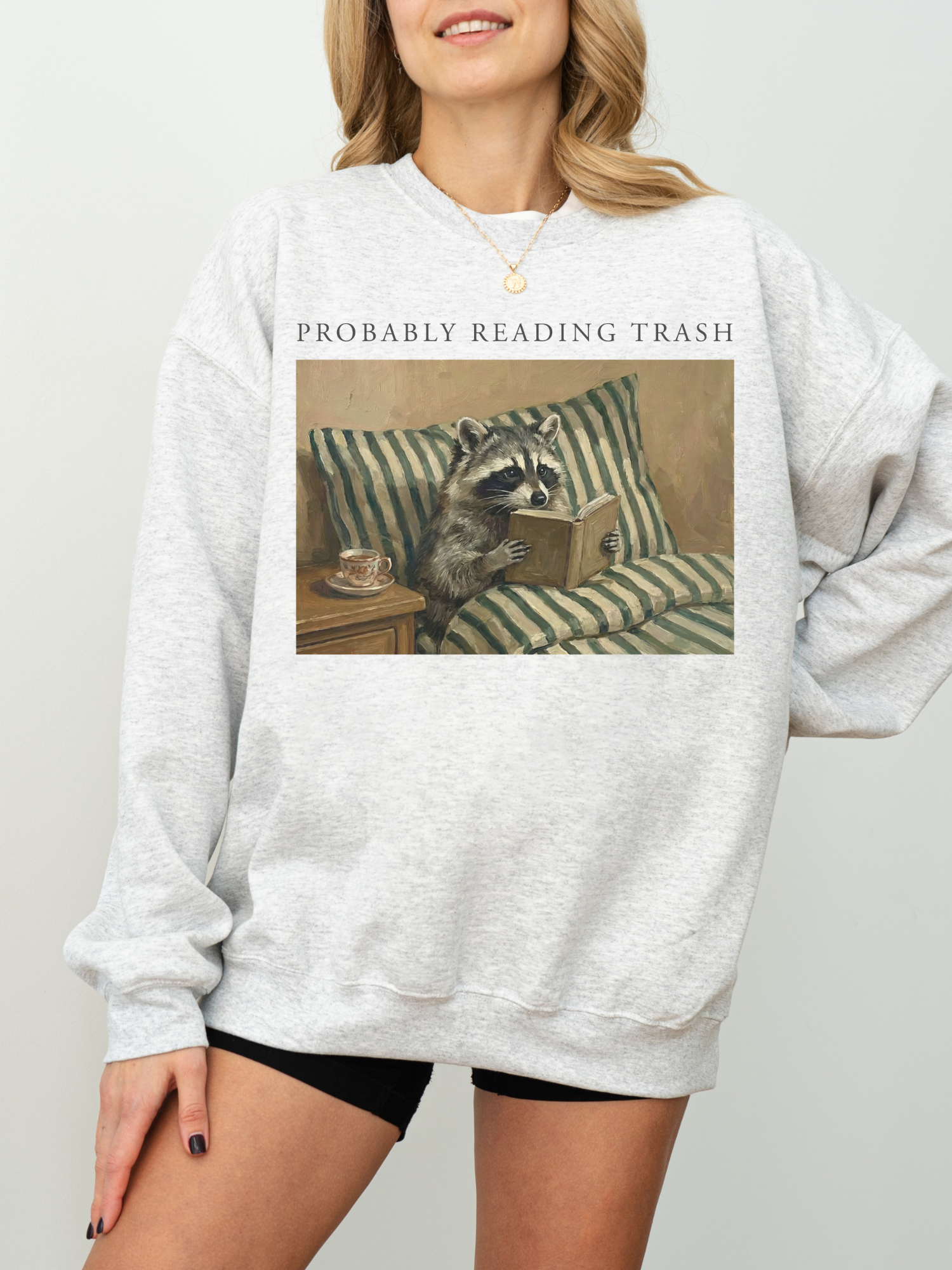 woman wearing oversized grey sweatshirt featuring probably reading trash raccoon reading book illustration relaxed fit cozy bookish outfit