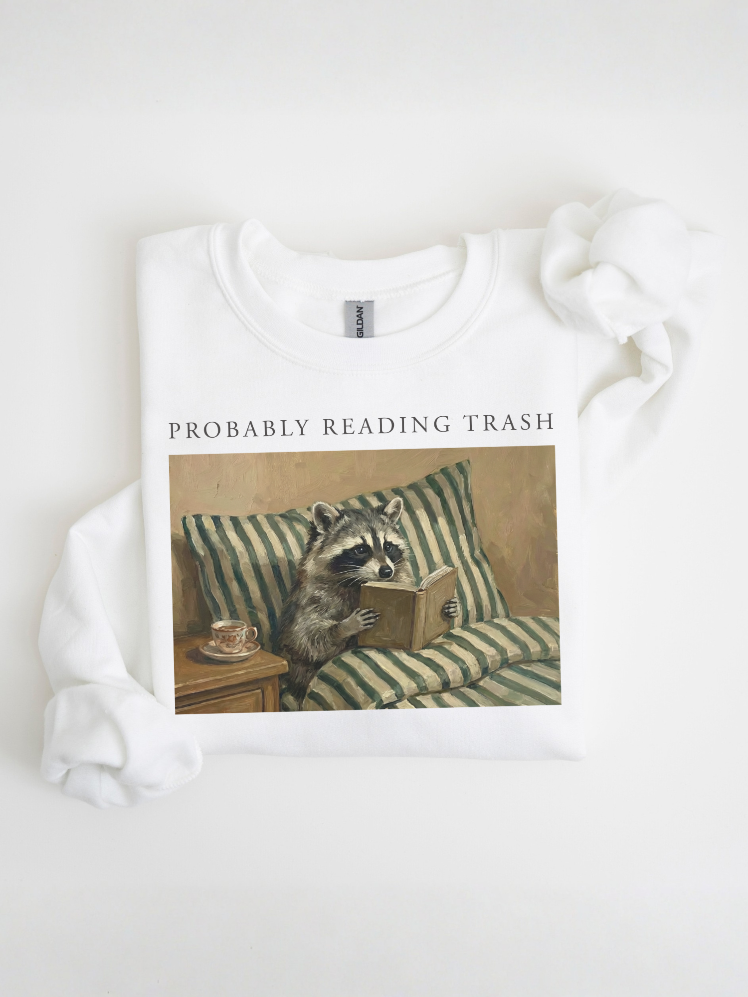 folded white sweatshirt with probably reading trash raccoon reading book graphic minimal aesthetic product flatlay