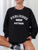 woman sitting cross-legged wearing black sweatshirt that says published author est 2012