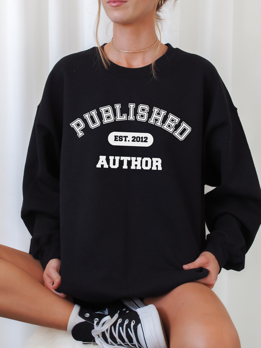 woman sitting cross-legged wearing black sweatshirt that says published author est 2012