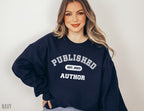 woman wearing navy sweatshirt that says published author est 2023, standing with hand on hip