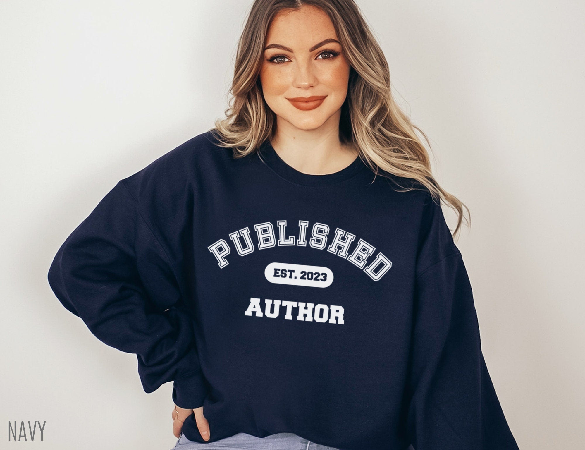 woman wearing navy sweatshirt that says published author est 2023, standing with hand on hip