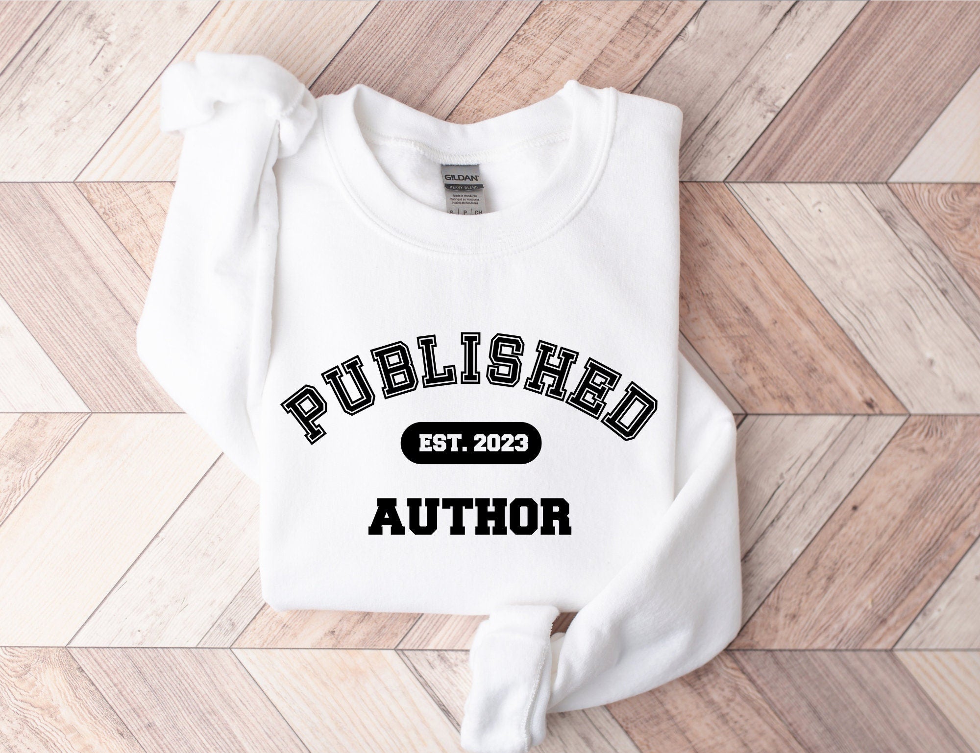 folded white sweatshirt that says published author est 2023 on chevron wood background