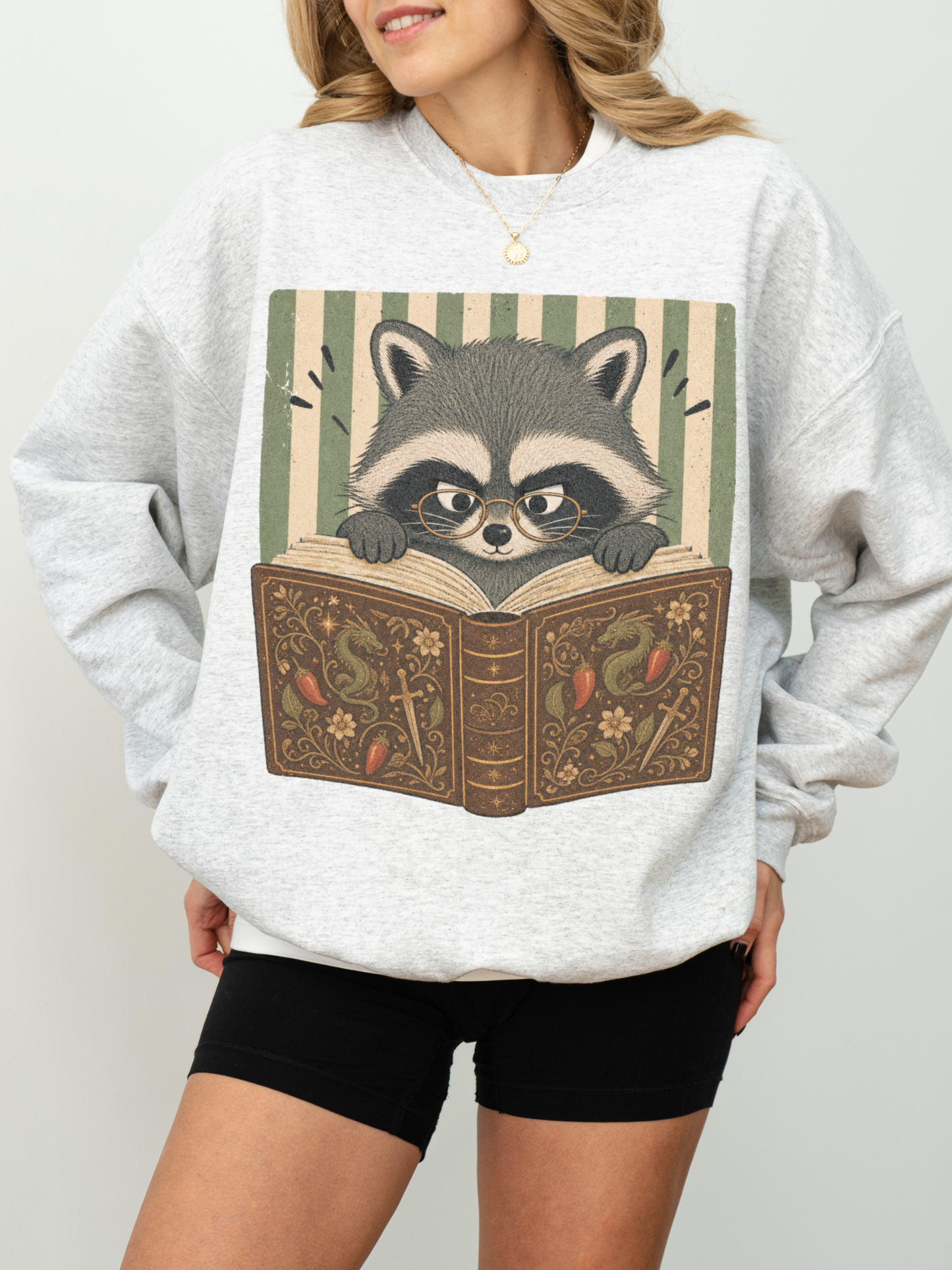 woman wearing ash gray Gildan raccoon reading book sweatshirt with vintage bookish raccoon and fantasy book graphic