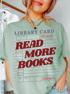 woman wearing a bay Comfort Colors shirt featuring a vintage library card graphic with the phrase read more books in bold red lettering, styled with layered gold necklaces and casual denim for a cozy book lover aesthetic