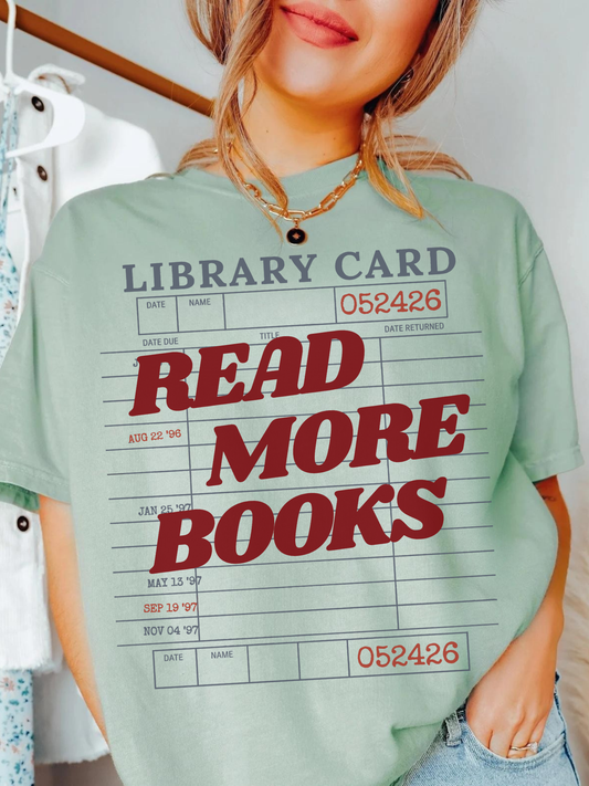 woman wearing a bay Comfort Colors shirt featuring a vintage library card graphic with the phrase read more books in bold red lettering, styled with layered gold necklaces and casual denim for a cozy book lover aesthetic