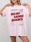 woman wearing a blossom pink Comfort Colors shirt featuring a library card inspired read more books graphic in red lettering, oversized book lover tee styled with biker shorts and gold jewelry
