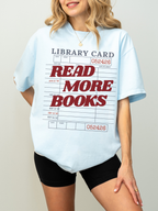 woman wearing a chambray blue Comfort Colors shirt featuring a vintage library card design with read more books text in bold red lettering, relaxed oversized fit for readers librarians and bookworms