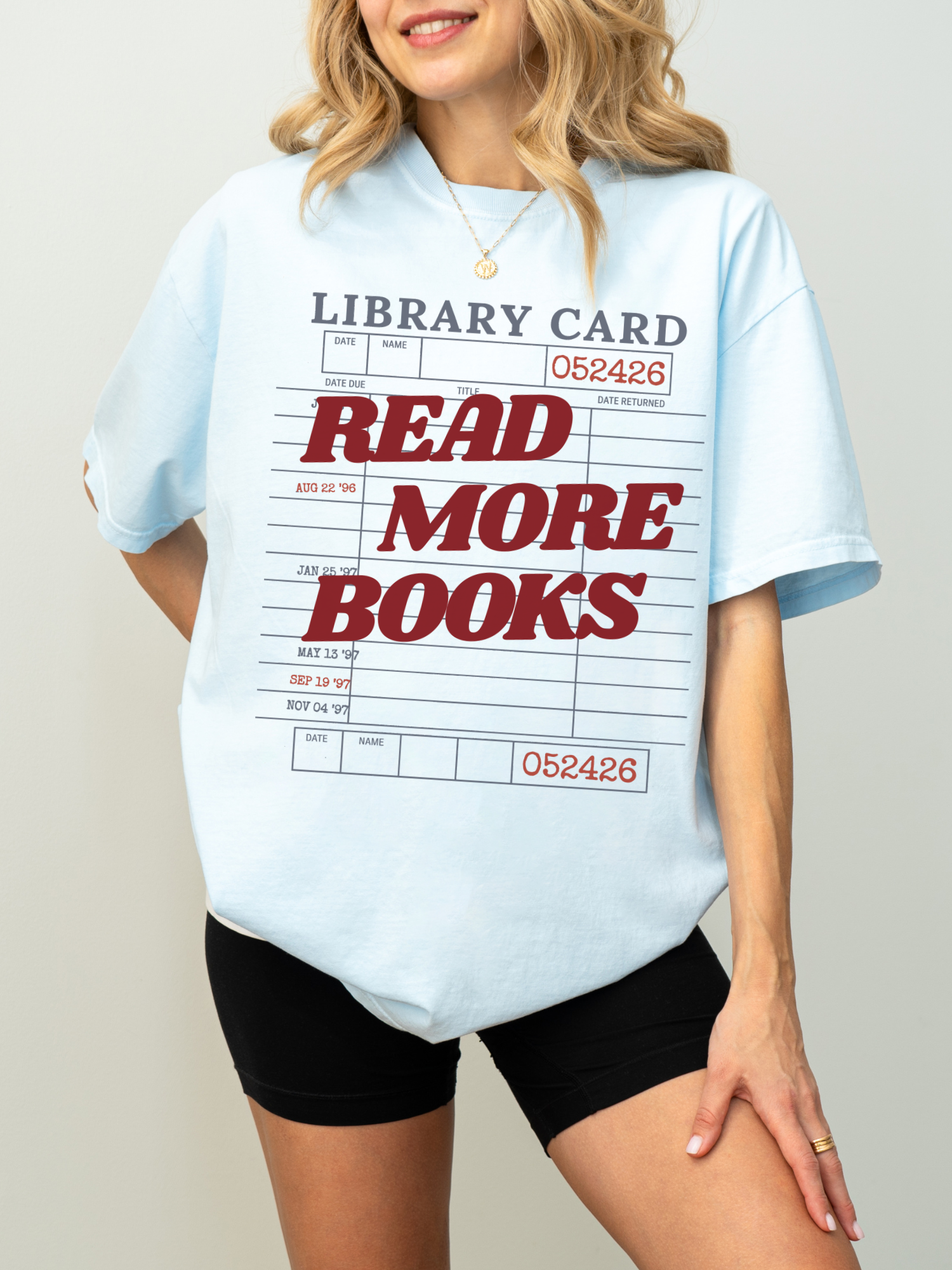 woman wearing a chambray blue Comfort Colors shirt featuring a vintage library card design with read more books text in bold red lettering, relaxed oversized fit for readers librarians and bookworms