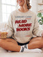 woman sitting with an iced coffee wearing a sweatshirt that says "read more books"