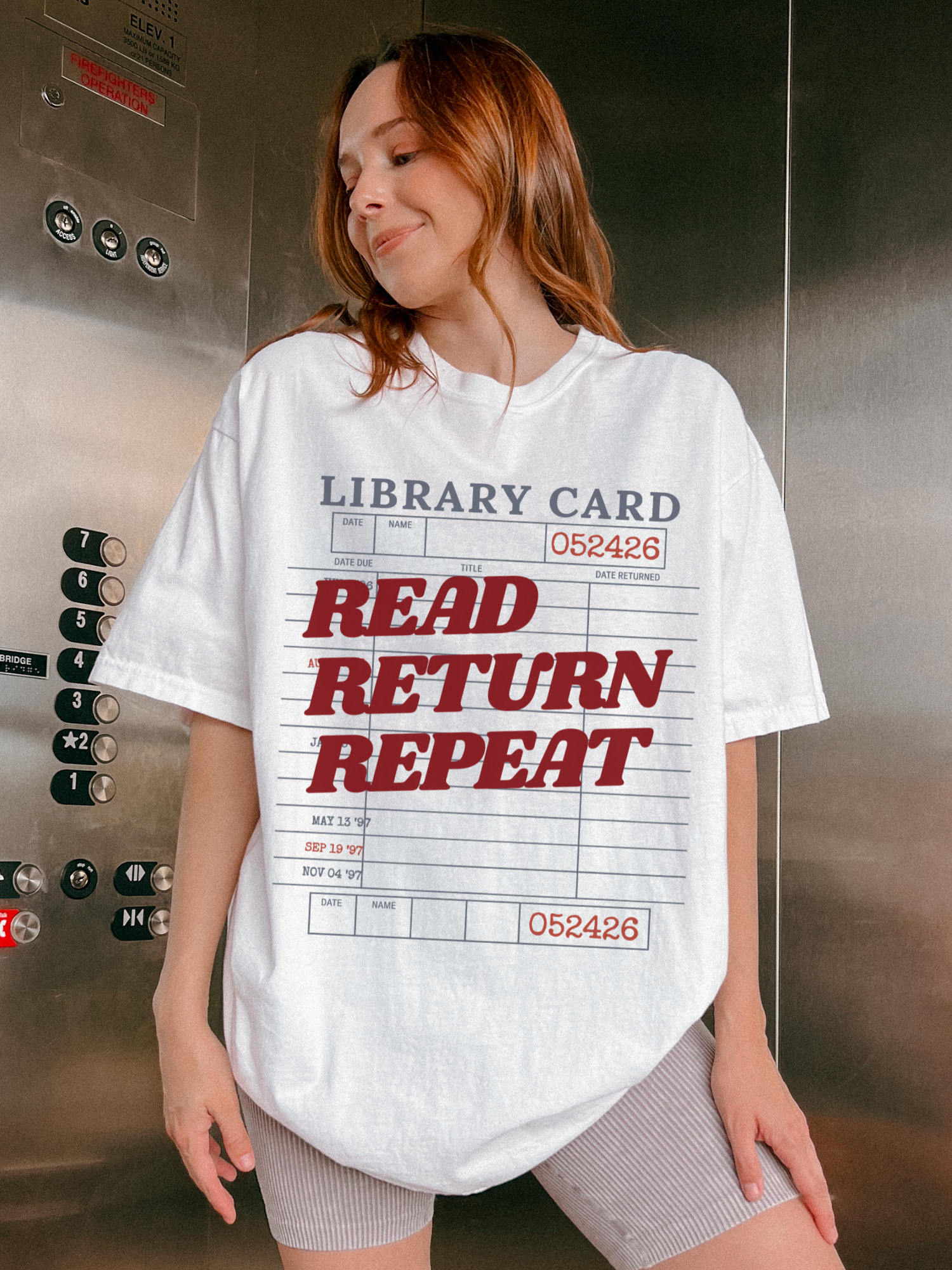 woman wearing a white Comfort Colors shirt featuring a vintage library card read return repeat design in an elevator setting, oversized reader graphic tee perfect for librarians bookworms and reading enthusiasts