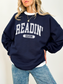 Navy sweatshirt with Readin' Season in light grey varsity text, worn over a white shirt and styled with relaxed denim
