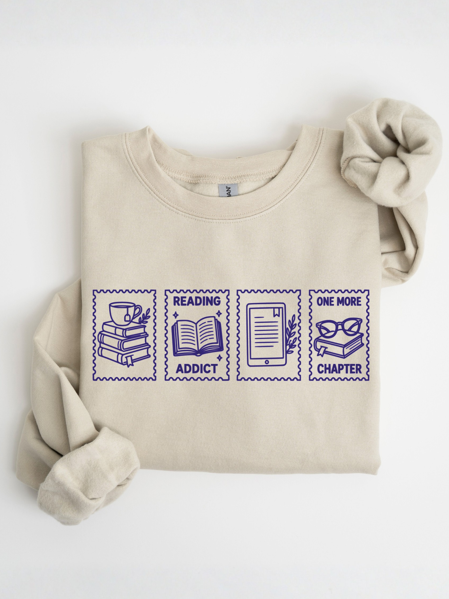 folded sand sweatshirt featuring reading addict one more chapter postage stamp style design with stack of books coffee cup open book e reader and reading glasses artwork