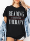 black comfort colors reading is cheaper than therapy shirt with minimalist typography design styled with denim jacket and shorts
