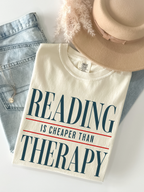 ivory comfort colors reading is cheaper than therapy shirt flat lay styled with denim jeans and beige hat aesthetic