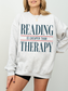 ash gray reading is cheaper than therapy sweatshirt for book lovers featuring minimalist typography design on cozy oversized crewneck