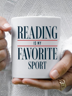 Close up of a white ceramic mug that says reading is my favorite sport in bold serif text, held with both hands by a person wearing a cozy knit sweater, creating a warm and relaxed reading aesthetic. The mug is styled for book lovers and readers, perfect for coffee or tea during quiet reading time at home.