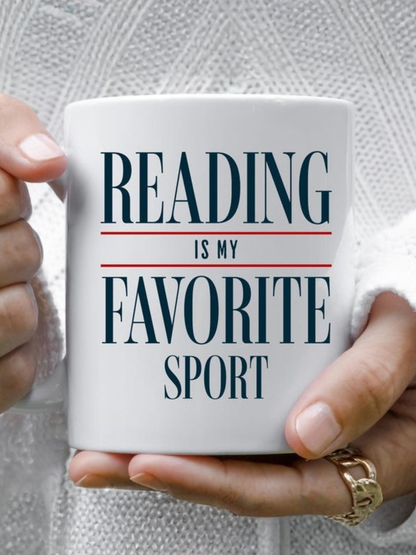 Close up of a white ceramic mug that says reading is my favorite sport in bold serif text, held with both hands by a person wearing a cozy knit sweater, creating a warm and relaxed reading aesthetic. The mug is styled for book lovers and readers, perfect for coffee or tea during quiet reading time at home.