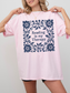 A woman wearing an oversized blossom t-shirt with a navy blue floral border and the text 'Reading is my Therapy' printed on the front, set against a plain light gray background.