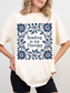 A woman wearing an oversized ivory-colored t-shirt with a navy blue floral border and the text 'Reading is my Therapy' printed on the front, paired with black shorts.