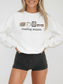 White reading season sweatshirt with minimalist book, mug, e-reader, and glasses illustrations, styled by a smiling woman in black shorts — comfy and clean book lover aesthetic.