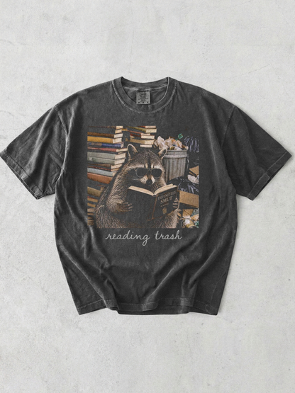 pepper comfort colors reading trash shirt featuring raccoon wearing sunglasses reading smut novel surrounded by books and trash cans