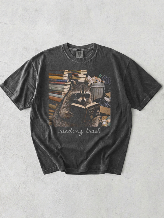 pepper comfort colors reading trash shirt featuring raccoon wearing sunglasses reading smut novel surrounded by books and trash cans