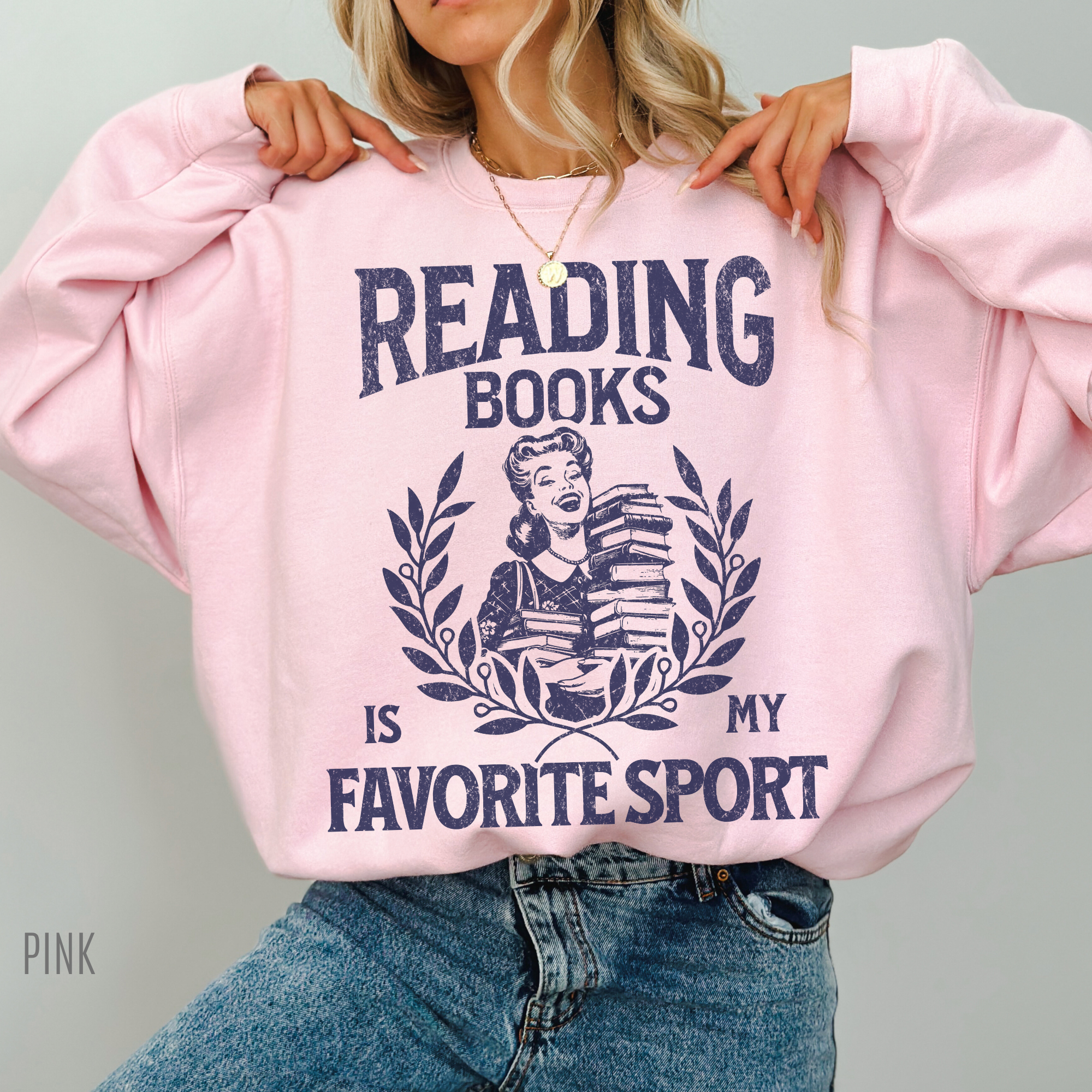 woman wearing a pink sweatshirt that says reading books is my favorite sport with retro style bookish graphic