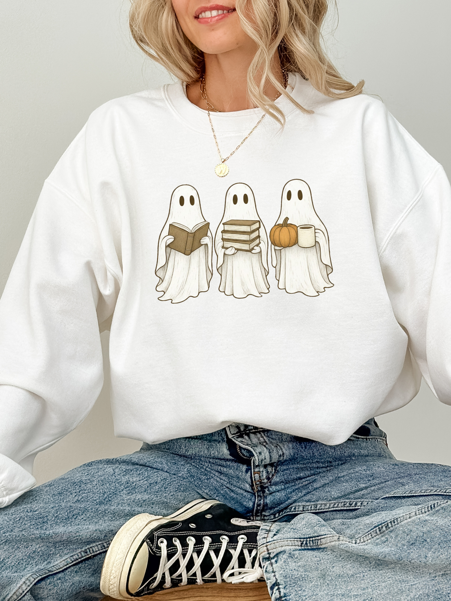 woman sitting cross-legged in a white sweatshirt with three reading ghosts design, perfect for Halloween and book lovers