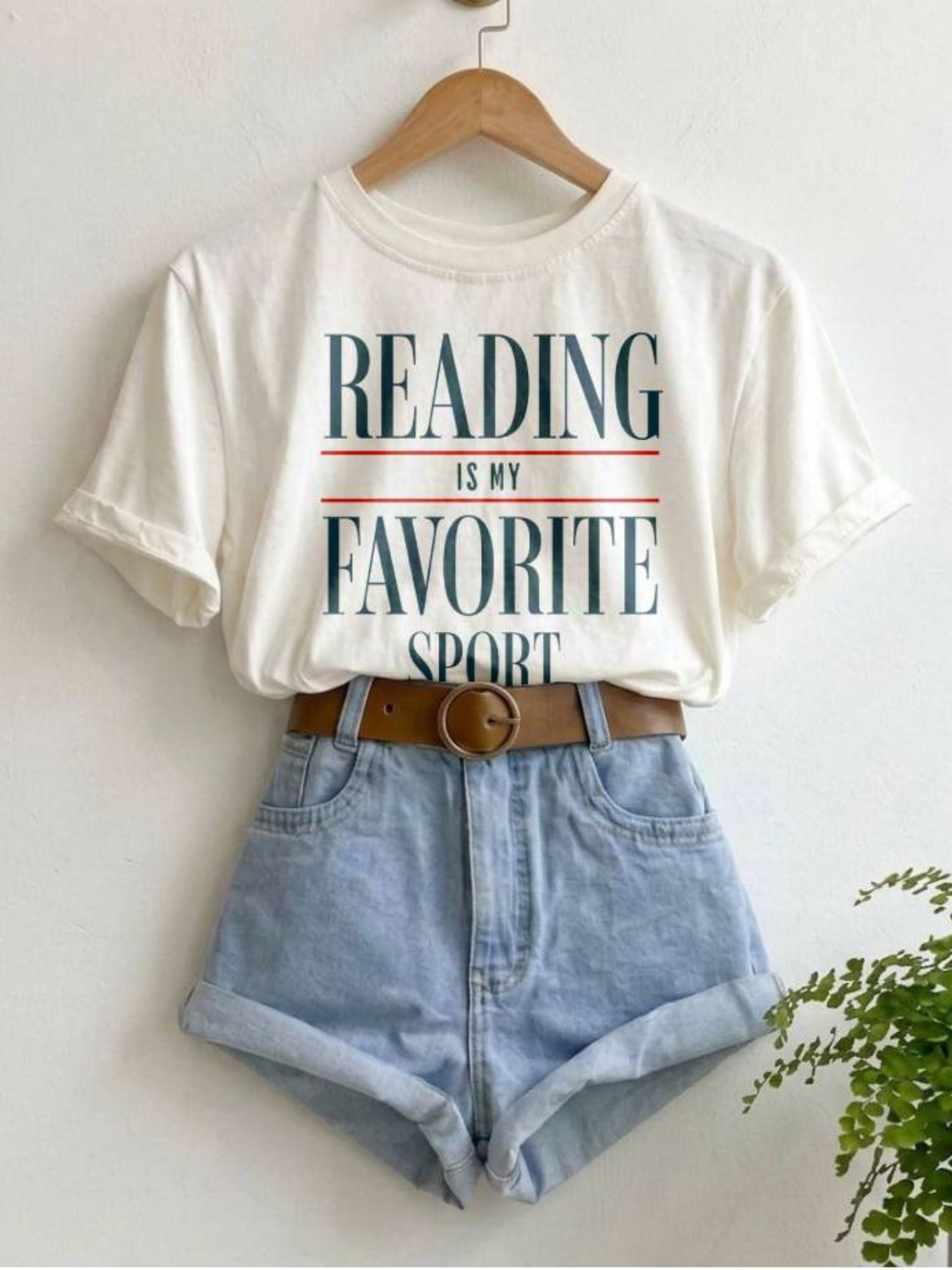a white shirt hanging on the wall with a vintage text that says "reading is my favorite sport"