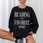 woman sitting cross-legged in black sweatshirt with bold white and red reading is my favorite sport print