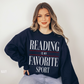 woman in navy reading is my favorite sport sweatshirt sitting on floor with relaxed bookish vibe