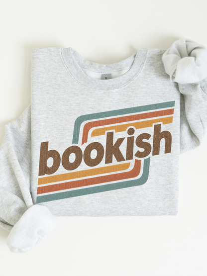 An ash gray crewneck sweatshirt with a retro-style graphic on the front. The graphic features the word 'bookish' in brown lowercase letters, layered over retro horizontal stripes in teal, orange, and brown.