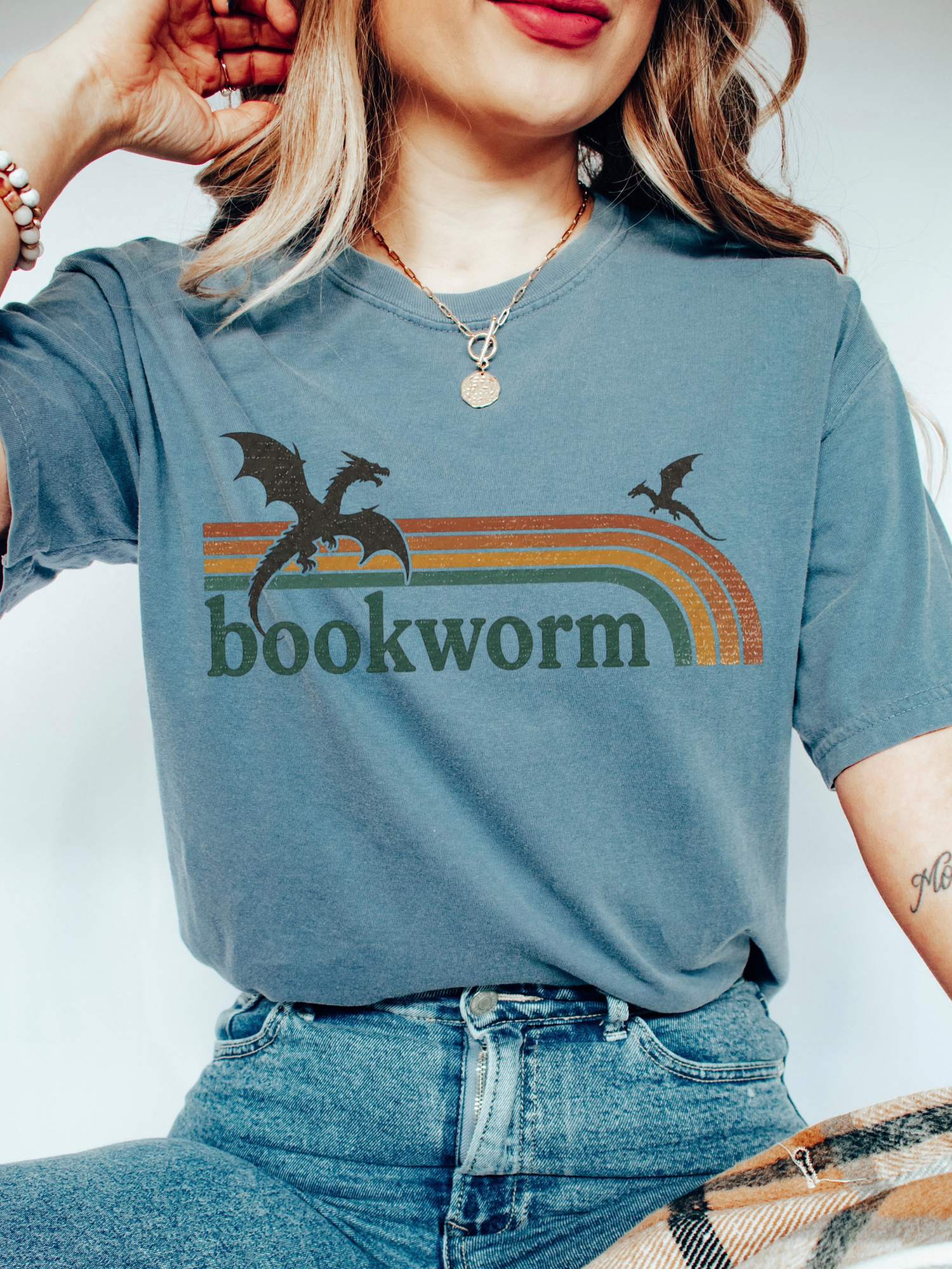 woman wearing blue jean comfort colors dragon bookworm shirt featuring vintage rainbow stripes and fantasy reader aesthetic graphic