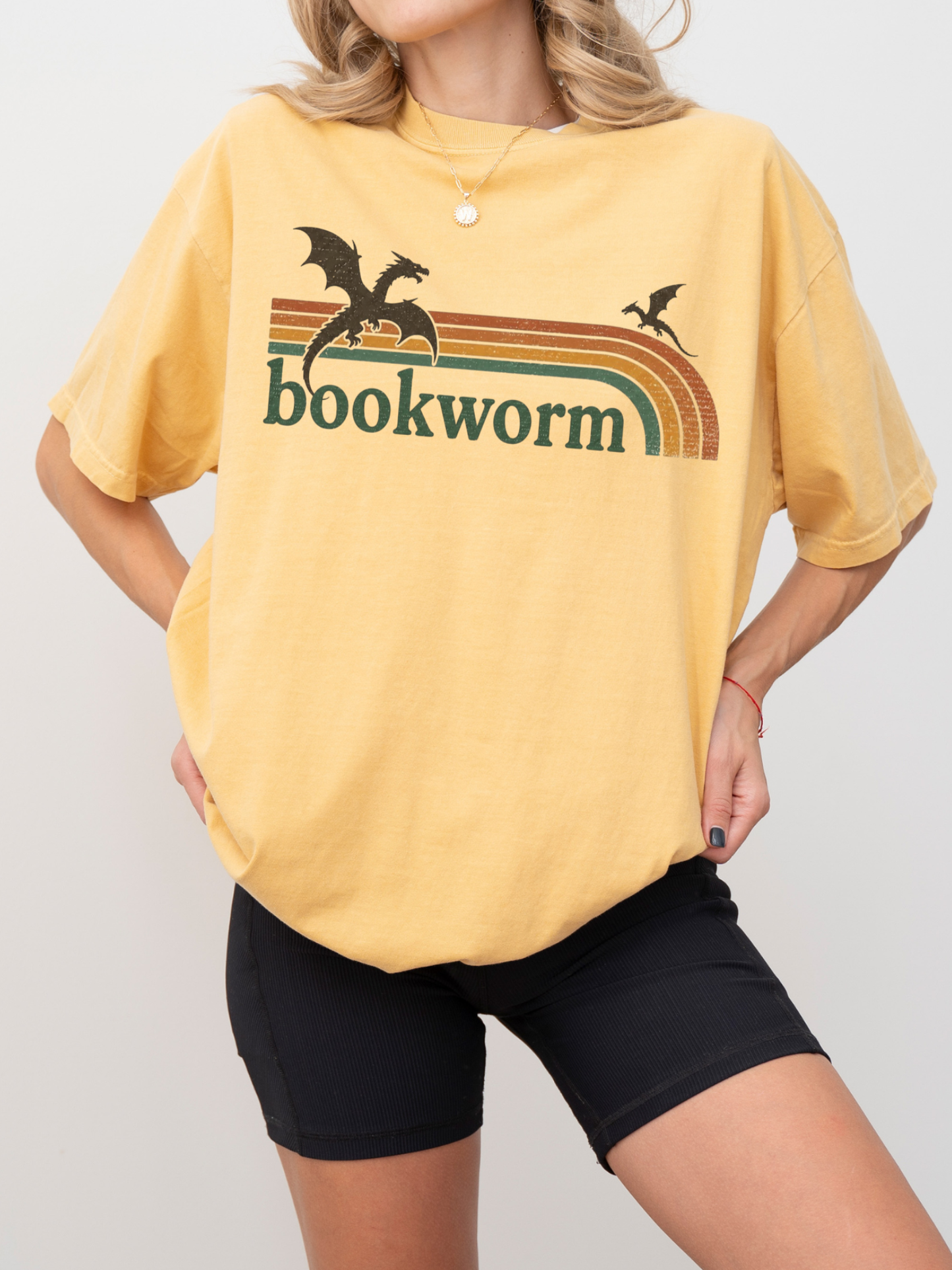 woman wearing mustard comfort colors fantasy bookworm shirt with retro rainbow design and black dragon book lover artwork