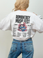 Back view of a light ash gray sweatshirt with bold "Romantasy Music Fest" graphic, featuring a skull and book stack surrounded by flowers and a lineup of fantasy romance tropes like enemies to lovers and assassin MCs.
