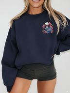 Woman wearing a navy crewneck sweatshirt with a small skull and book stack design printed on the left chest, styled with black shorts and tousled hair for a casual and cozy bookish aesthetic.