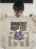 Sand-colored sweatshirt laid flat with the Romantasy Music Fest concert-style graphic on the back, listing iconic romantasy tropes like found family, magic school, and grumpy sunshine alongside a skull and book stack design.