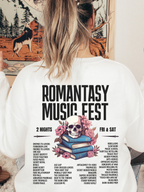 White sweatshirt with Romantasy Music Fest graphic on the back, including a pink floral skull atop books and fantasy tropes like morally grey men and found magic, modeled with loose waves in a cozy indoor setting.