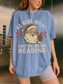 Woman wearing blue oversized Christmas t-shirt with vintage Santa and “He Sees What You’ve Been Reading” design, posing in elevator