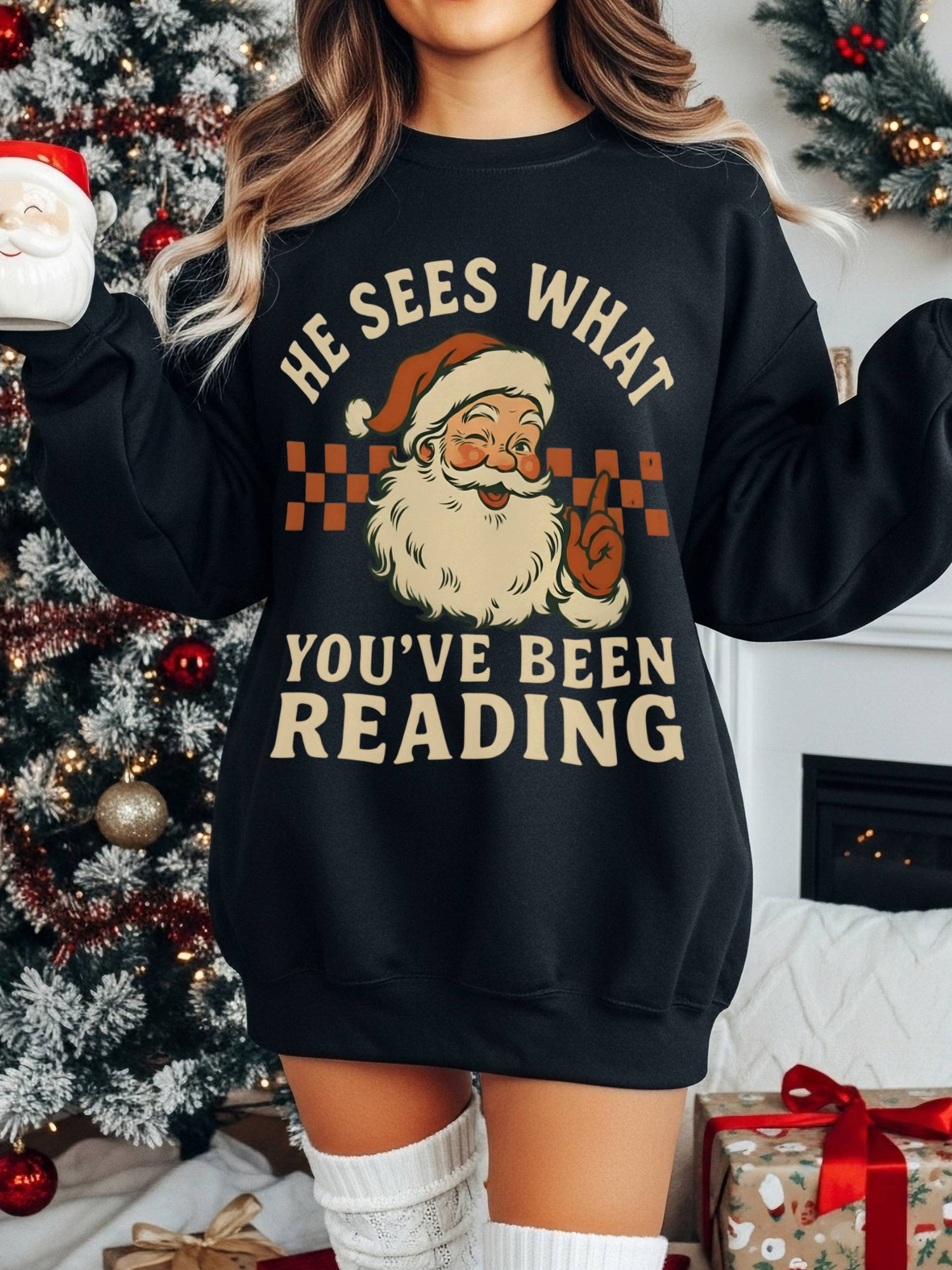 woman in black sweatshirt standing in front of Christmas tree holding Santa mug, festive background