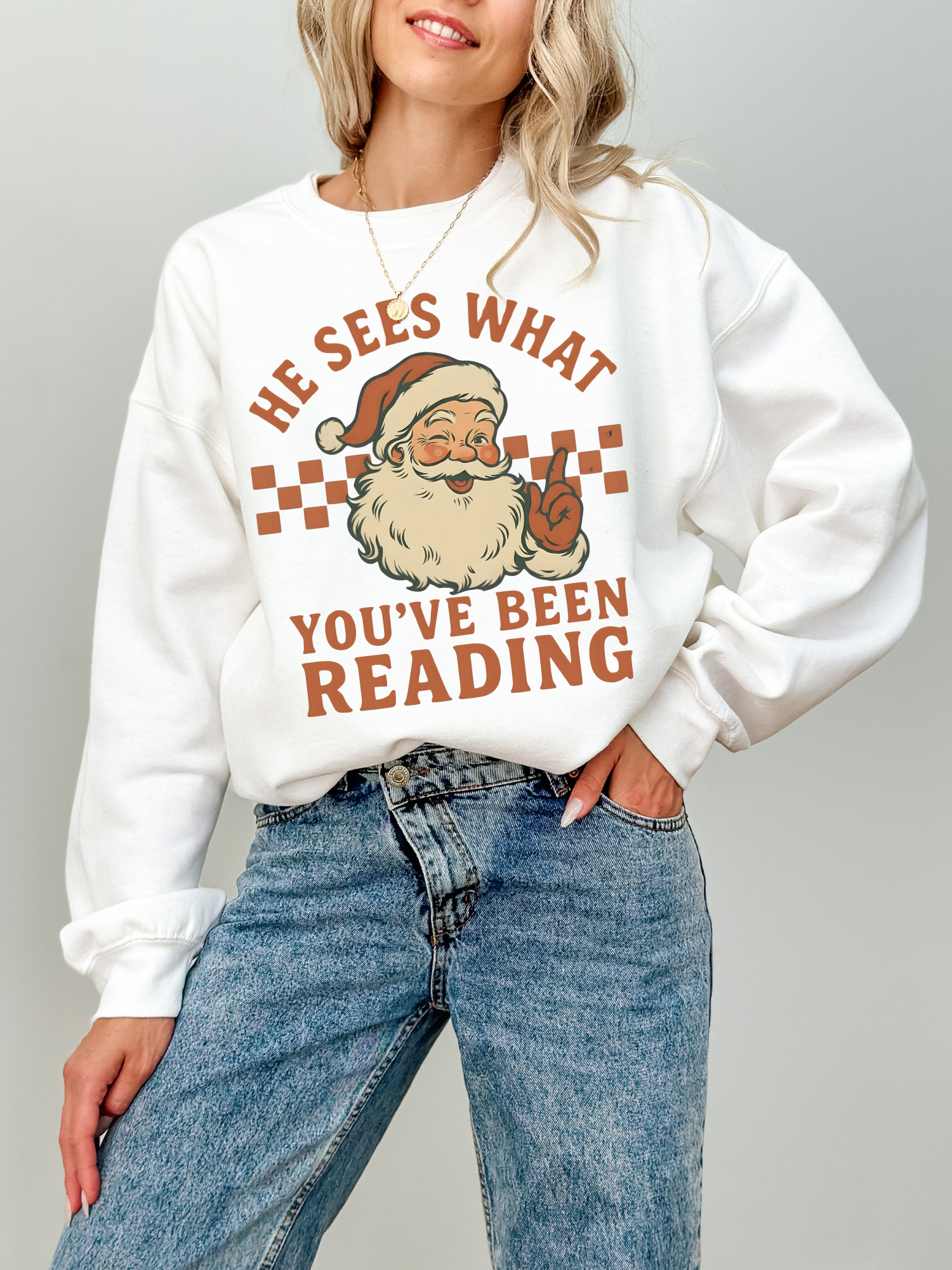 girl wearing white sweatshirt with vintage Santa and the words he sees what you've been reading
