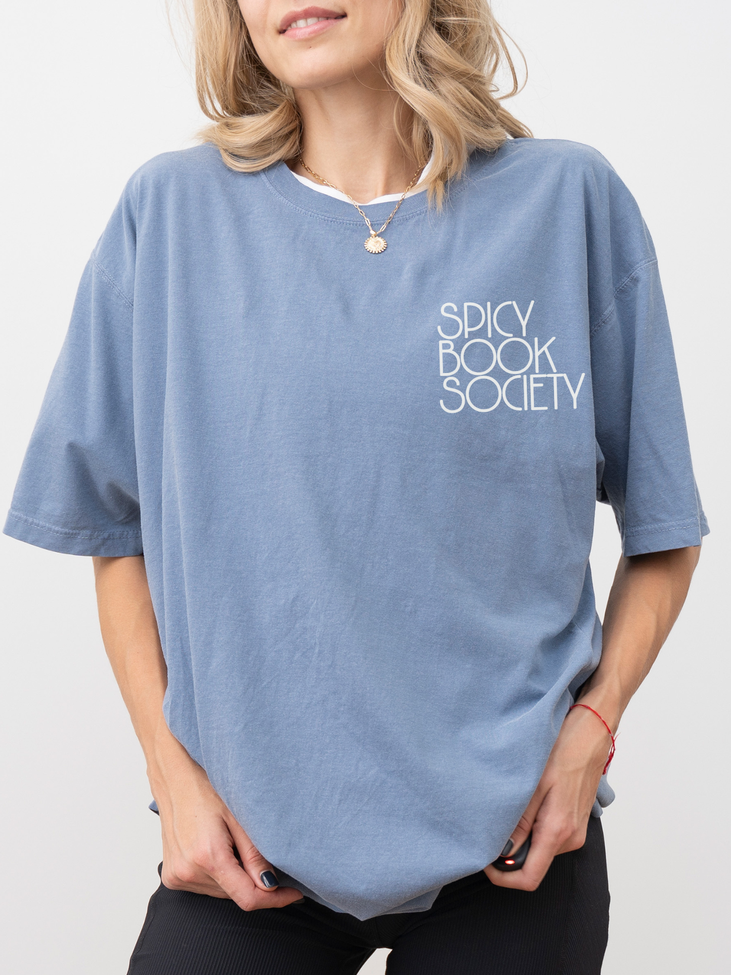 Smiling woman wearing a blue jean Comfort Colors tee with minimalist “Spicy Book Society” text. Styled in casual reader fashion with gold necklace and soft makeup, perfect for spicy book lovers and book club aesthetics.