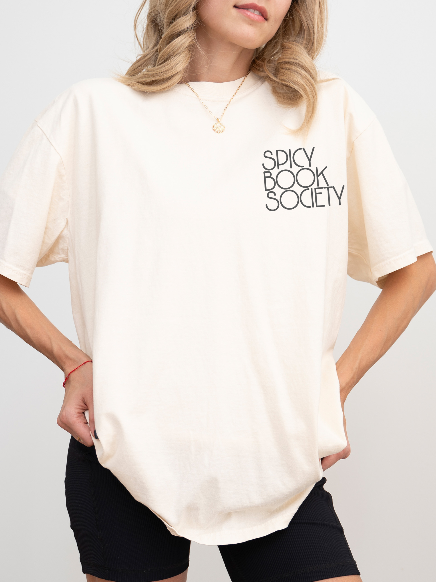 Model wearing a natural ivory Comfort Colors shirt with “Spicy Book Society” printed on the front chest. Styled in a clean, minimal look with biker shorts, soft waves, and gold jewelry — perfect for spicy fiction fans.