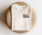 folded cream bookish t-shirt with spicy literature connoisseur text and pepper icon on wicker ottoman