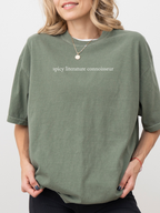 Close-up of moss Comfort Colors shirt featuring the phrase “spicy literature connoisseur,” worn by a blonde woman with soft curls.