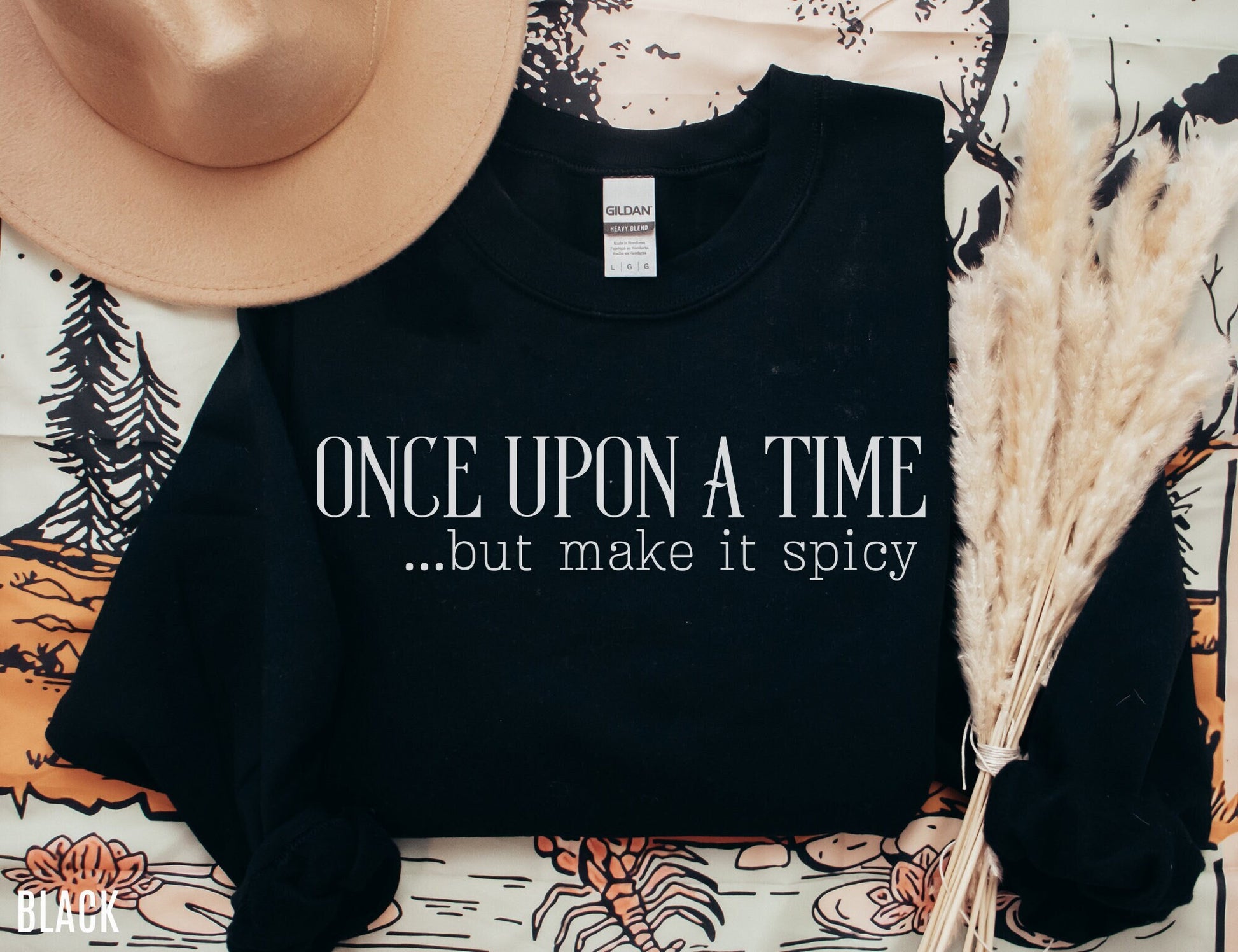 folded black sweatshirt on book-themed backdrop with text once upon a time but make it spicy