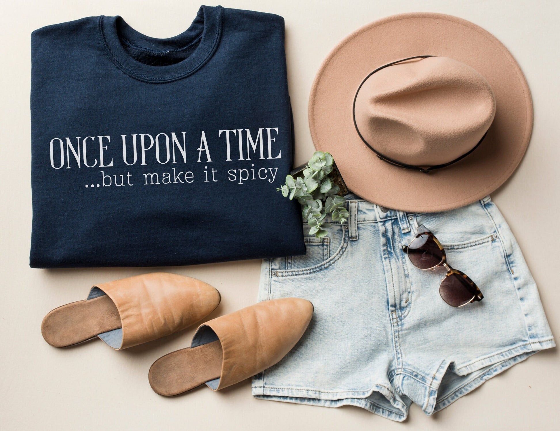 folded navy sweatshirt that says once upon a time but make it spicy, styled with tan hat and summer clothes