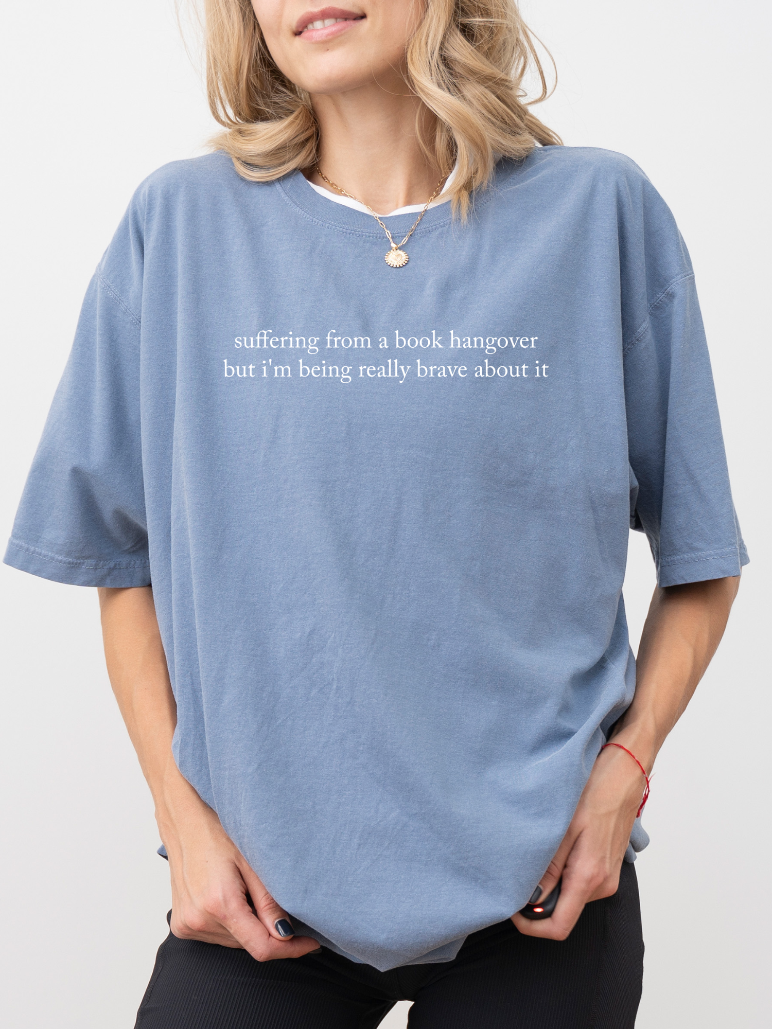 Woman wearing blue jean Comfort Colors book lover shirt that says suffering from a book hangover but i'm being really brave about it styled casually with necklace and relaxed fit tee