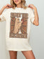 A woman wearing an oversized ivory-colored graphic t-shirt with a vintage-style print of a ghost reaching for a book on a library shelf, with the text 'SUPPORT YOUR LOCAL BOOKSTORE'.